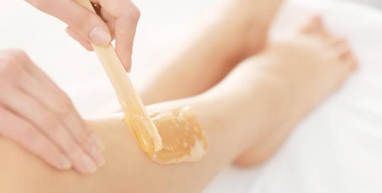 Hand applying warm wax with wooden spatula on lower leg for hair removal
