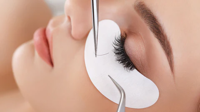 Close-up of a person receiving eyelash extension application with tweezers and under-eye pad