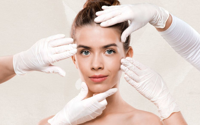 Young woman with clear skin surrounded by hands in white gloves framing her face