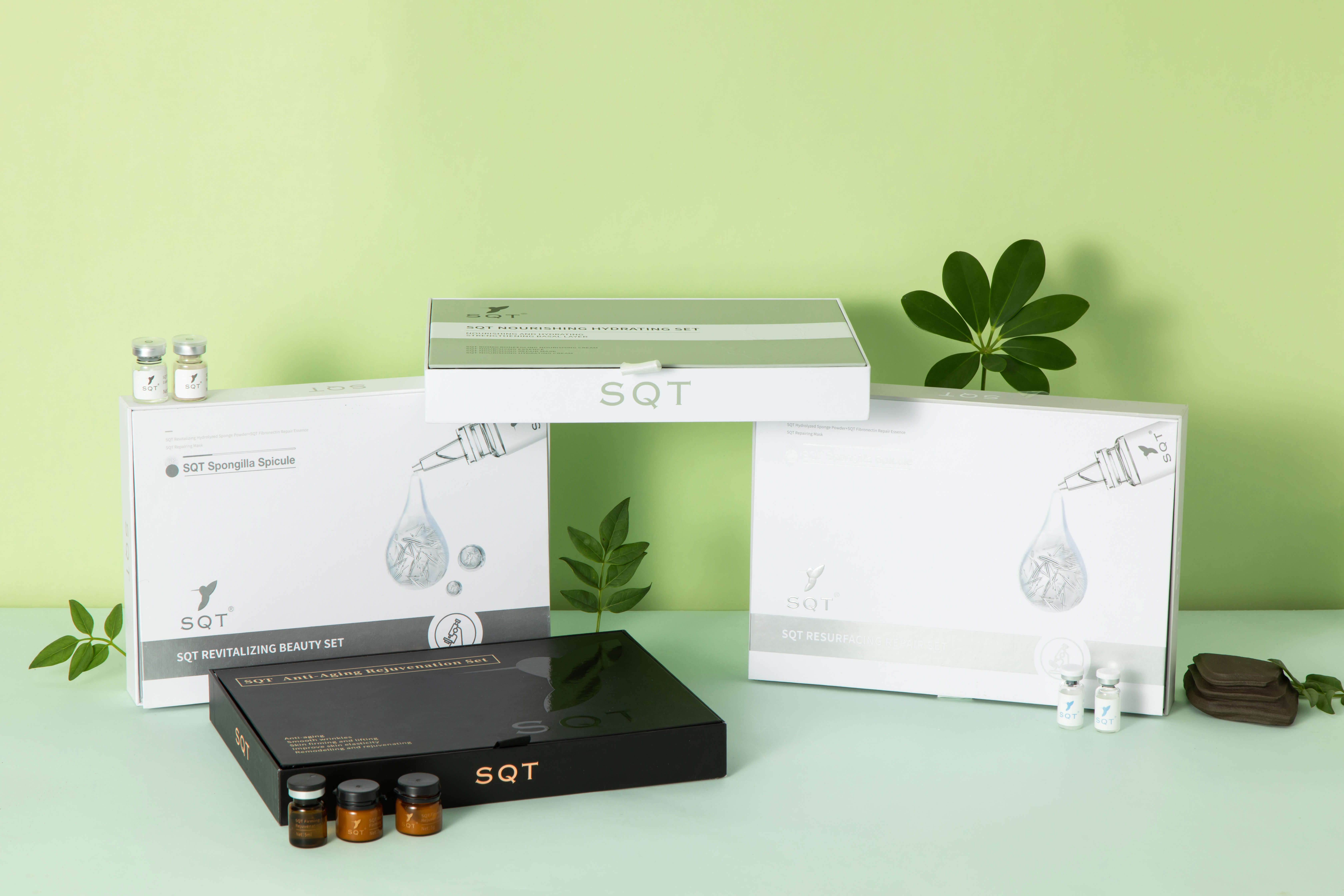SQT branded skincare sets and small vials displayed on a light green surface with green leaves