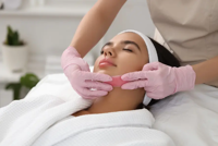 Woman receiving chin waxing treatment with pink wax strip by gloved hands