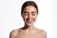 Young woman with clear skin smiling with eyes closed against white background