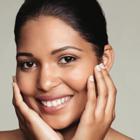 Smiling woman with clear skin gently touching her face with both hands