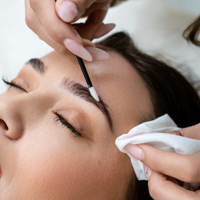 Close-up of a woman receiving eyebrow grooming with a small brush and cotton pad